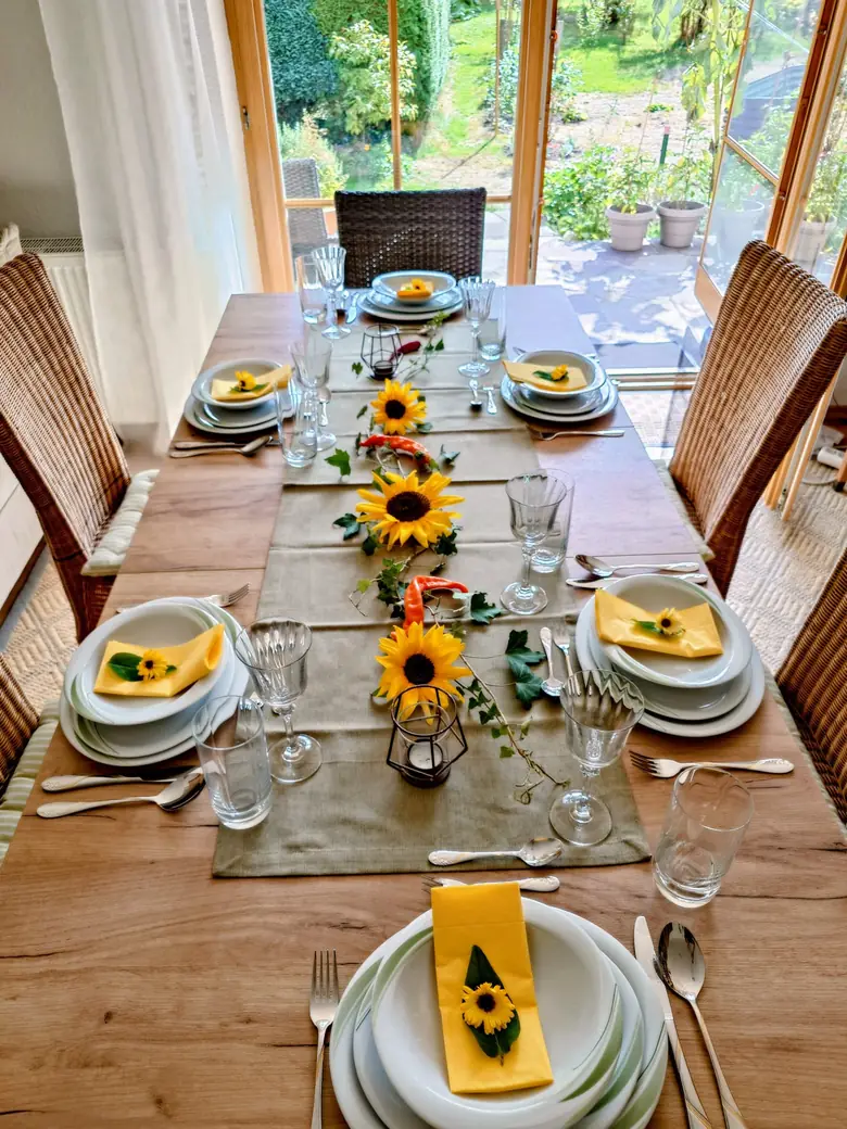 Gedeckter Tisch mit Sonnenblumen, Efeu und gelben Servietten, dahinter der Blick in den Garten